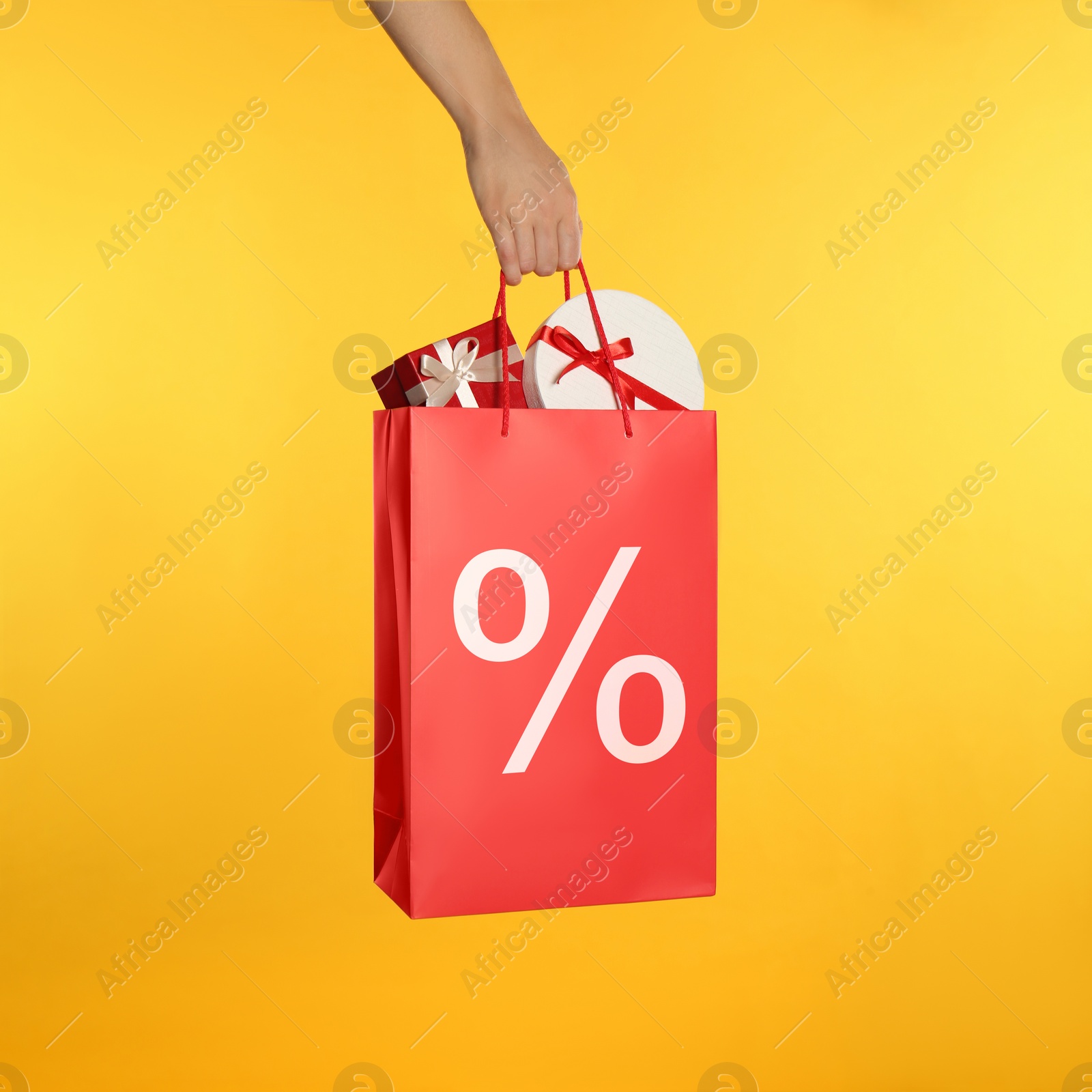 Image of Woman holding paper shopping bag with percent sign on yellow background, closeup. Discount concept