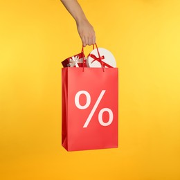 Image of Woman holding paper shopping bag with percent sign on yellow background, closeup. Discount concept