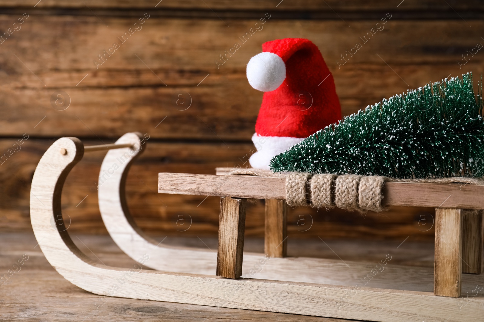 Photo of Sleigh with decorative Christmas tree and Santa hat on wooden table