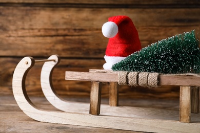 Photo of Sleigh with decorative Christmas tree and Santa hat on wooden table