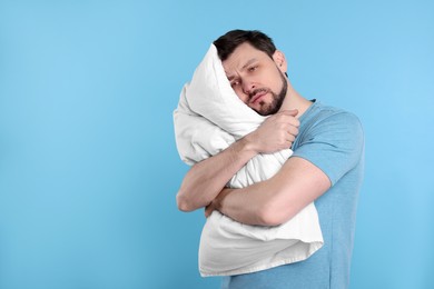 Photo of Tired man with pillow on light blue background, space for text. Insomnia problem