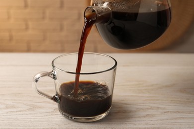 Photo of Pouring coffee into cup at light wooden table, closeup