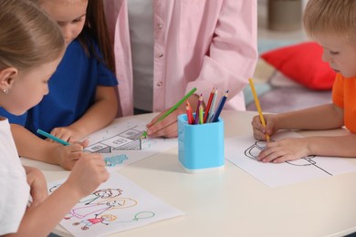 Photo of Nursery teacher and little children drawing pictures at desk in kindergarten, closeup. Playtime activities