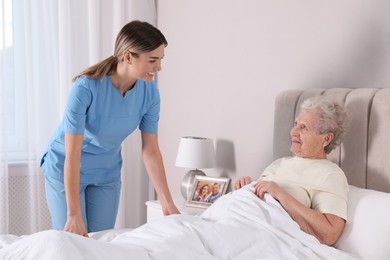 Photo of Young caregiver assisting senior woman in bedroom. Home health care service