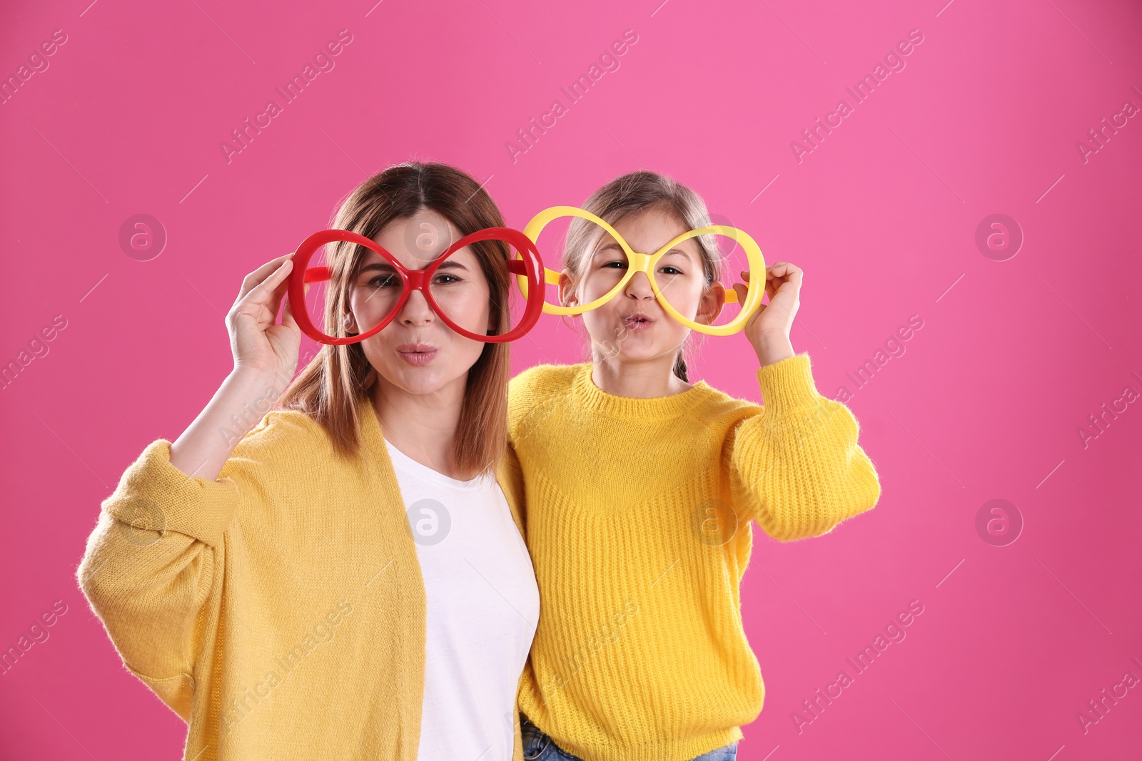 Photo of Happy woman and daughter with funny glasses on color background