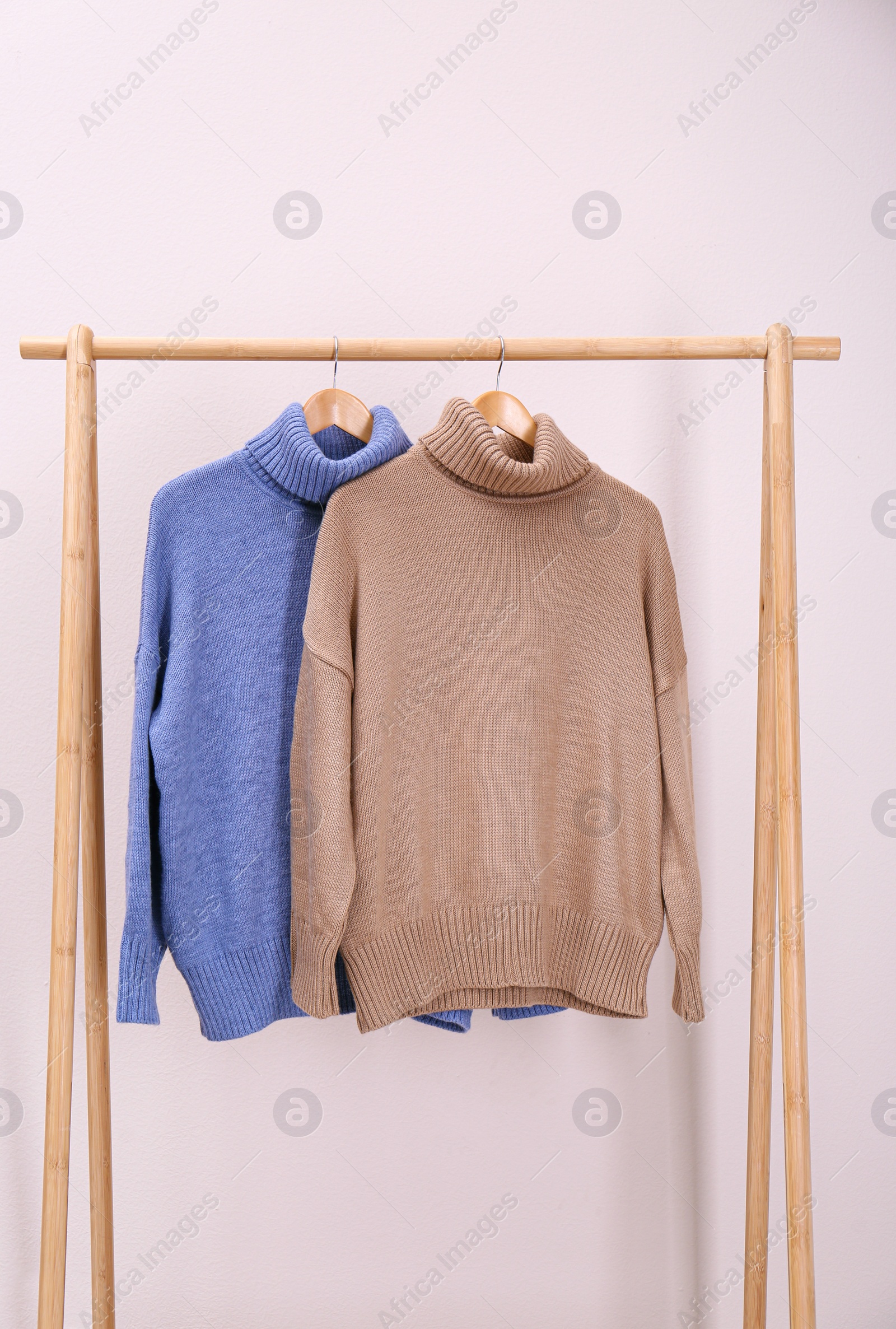 Photo of Stylish knitted sweaters hanging on clothing rack near pink wall