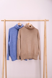 Stylish knitted sweaters hanging on clothing rack near pink wall