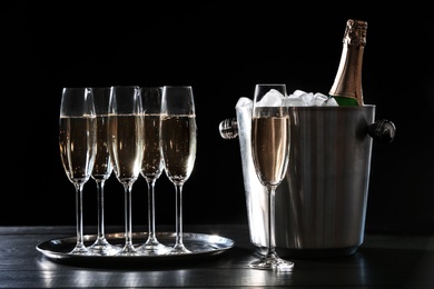 Photo of Glasses with champagne and bottle in bucket on dark table
