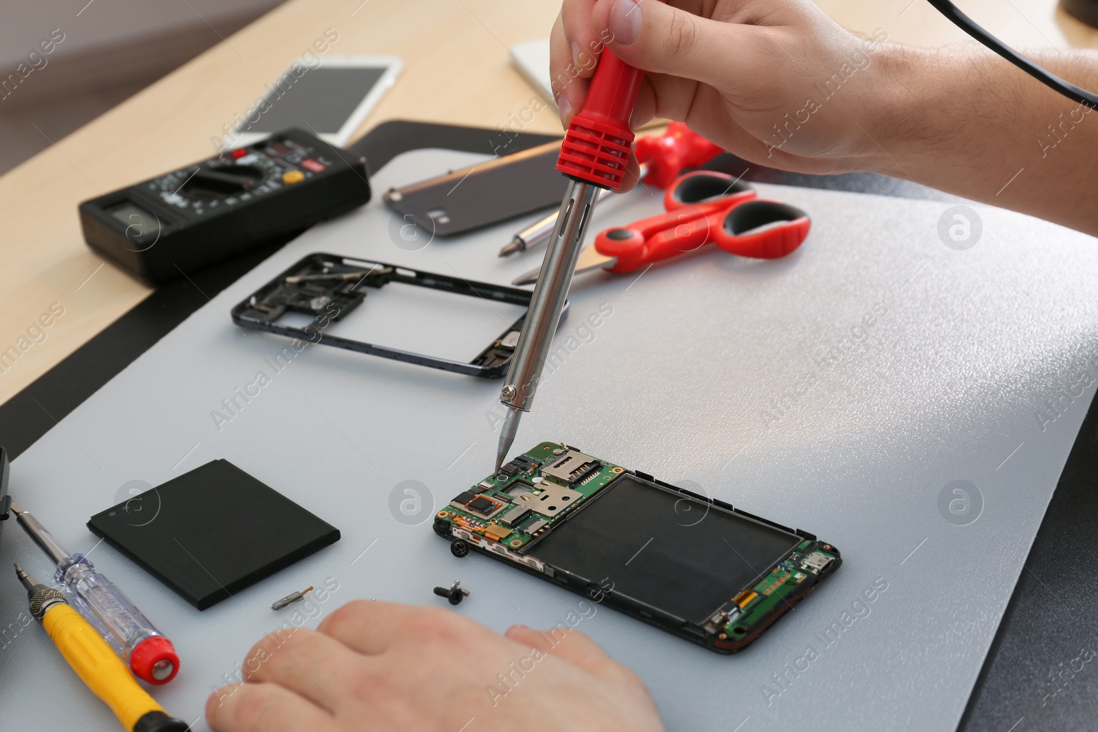 Photo of Technician repairing broken smartphone at table, closeup