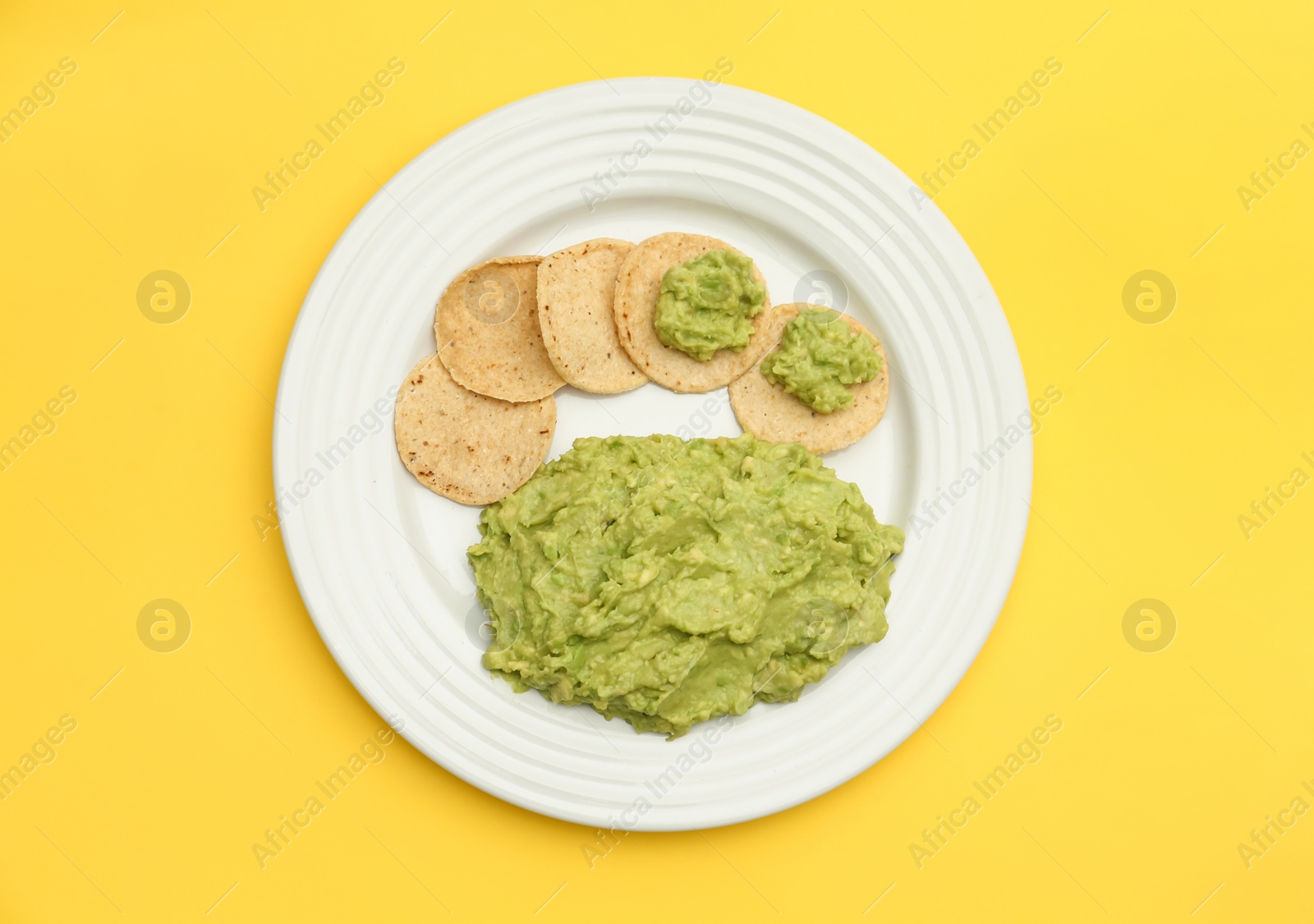 Photo of Delicious guacamole made of avocados and chips on yellow background, top view