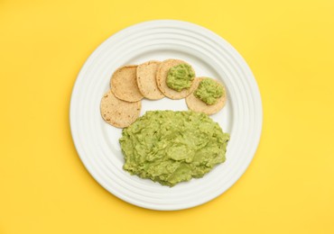 Photo of Delicious guacamole made of avocados and chips on yellow background, top view