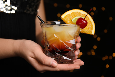 Photo of Woman with glass of Tequila Sunrise on blurred background, closeup. Delicious alcoholic cocktail