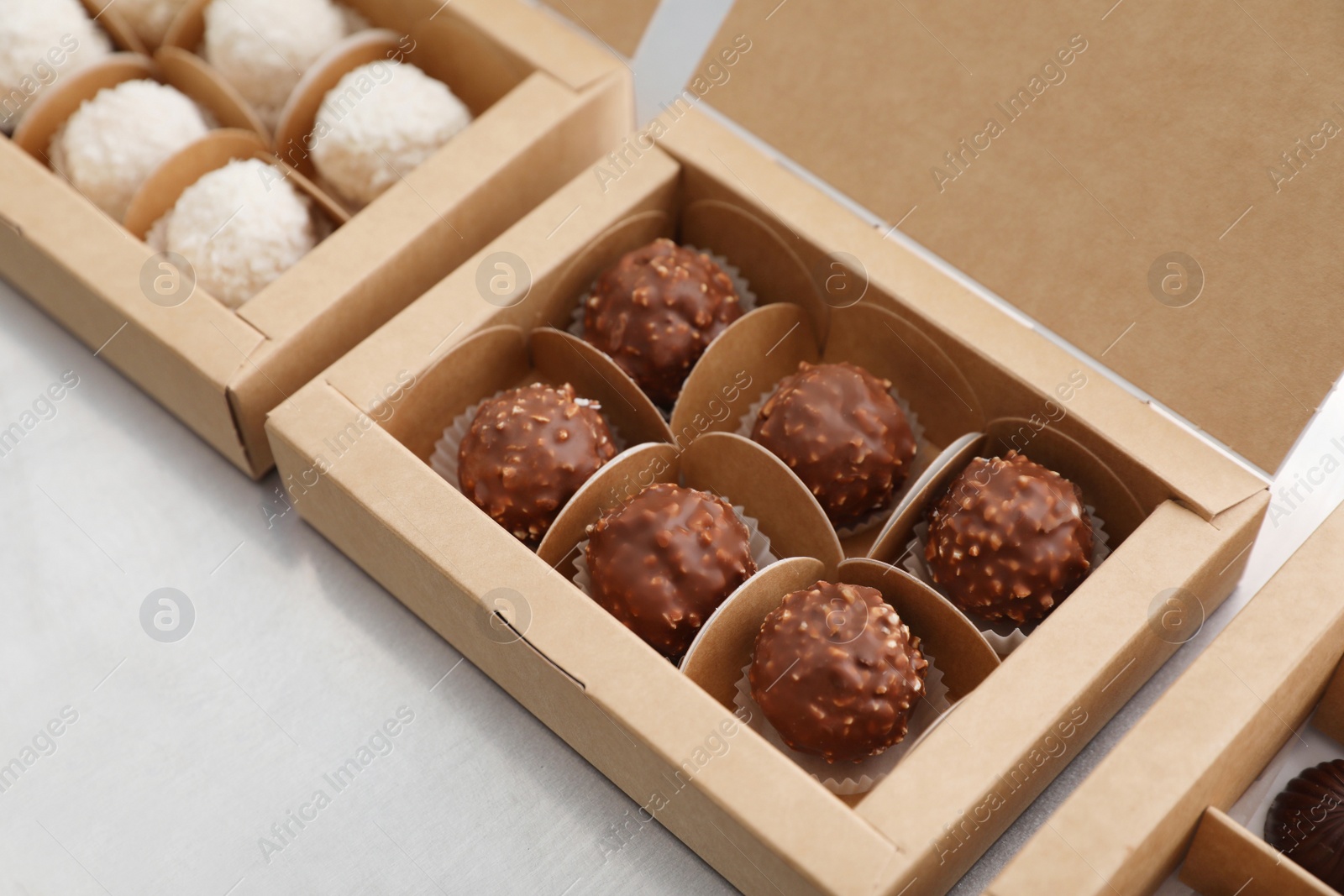 Photo of Different delicious chocolate candies and boxes on white table, closeup. Production line