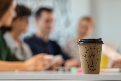 Photo of Team of employees working together in office. Paper cup of drink on white table, selective focus