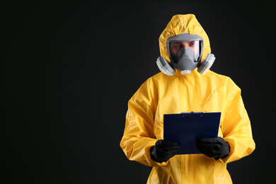 Photo of Man in chemical protective suit holding clipboard on black background, space for text. Virus research