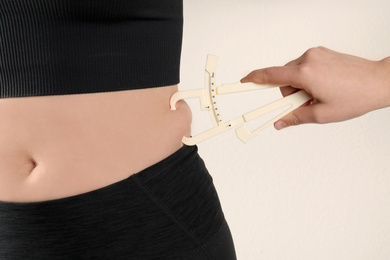 Photo of Nutritionist measuring woman's body fat layer with caliper on beige background, closeup
