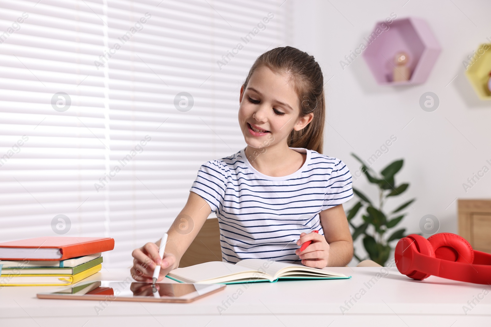 Photo of E-learning. Cute girl using tablet for studying online at table indoors