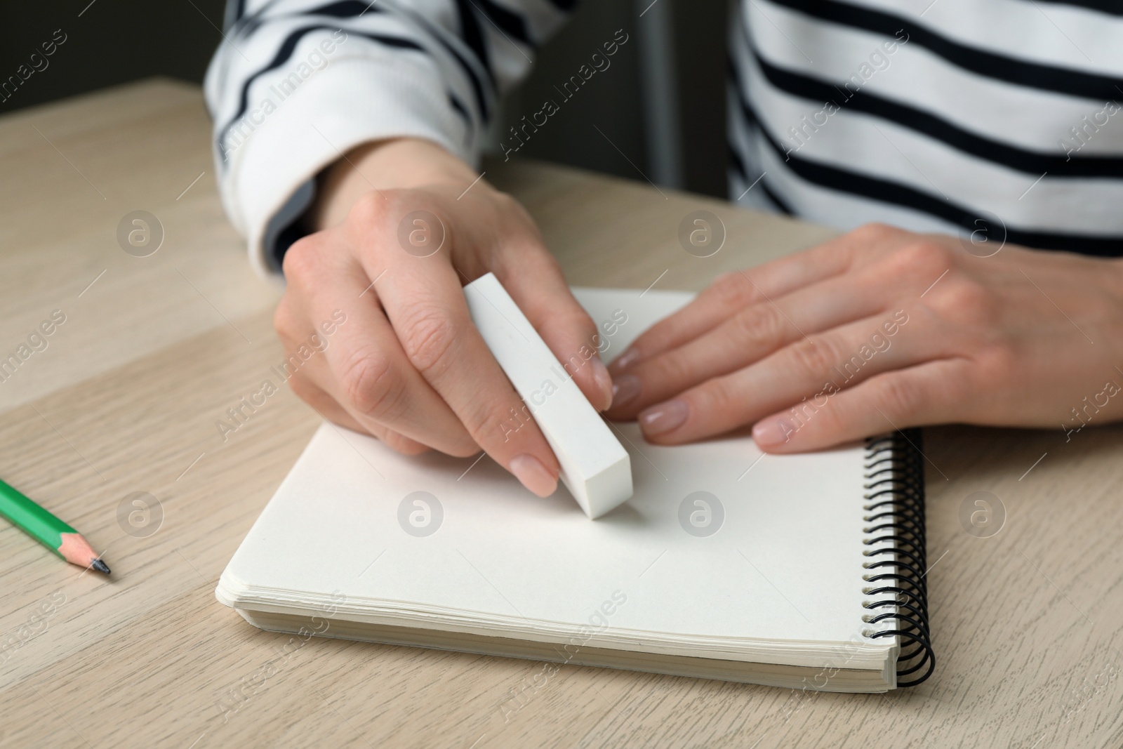 Photo of Woman erasing something in notebook at wooden table, closeup