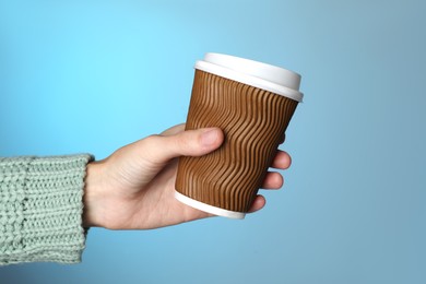 Photo of Woman holding takeaway paper coffee cup on blue background, closeup