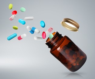 Many different colorful pills falling into bottle on light grey background