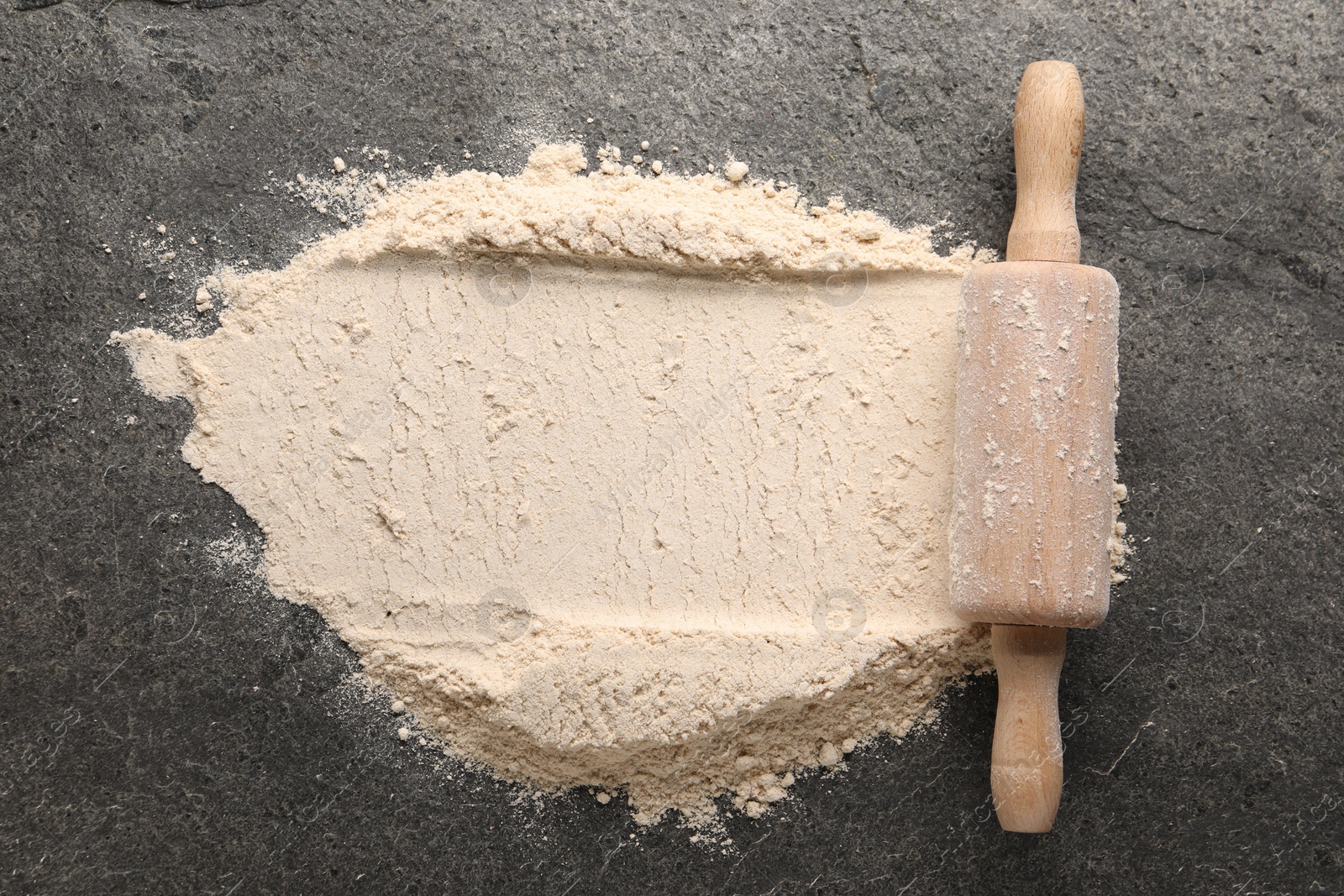 Photo of Scattered flour and rolling pin on grey textured table, top view