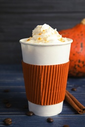 Photo of Takeaway paper cup with pumpkin spice latte and whipped cream on wooden table