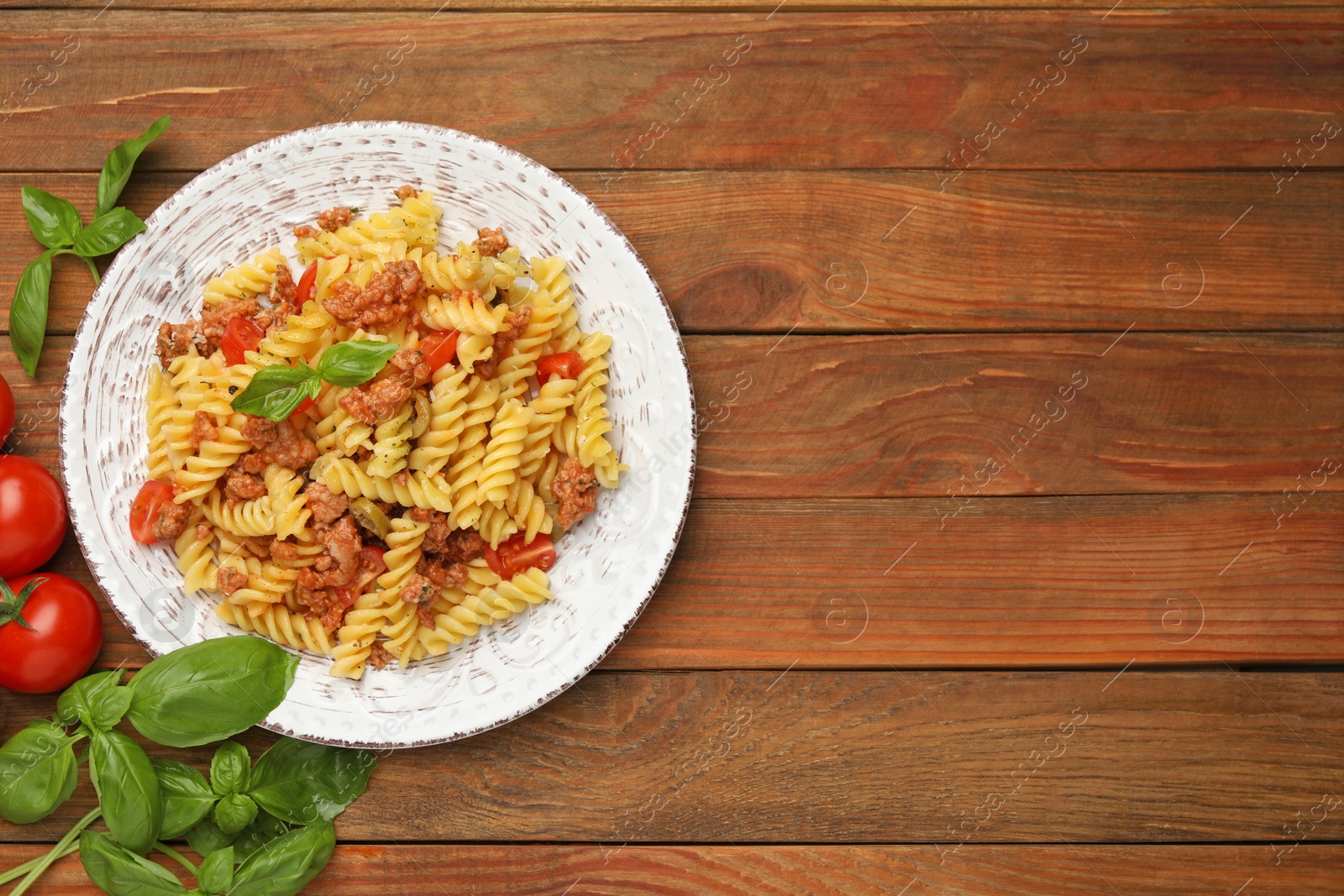 Photo of Plate of delicious pasta with minced meat, tomatoes and basil on wooden table, flat lay. Space for text