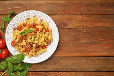 Photo of Plate of delicious pasta with minced meat, tomatoes and basil on wooden table, flat lay. Space for text