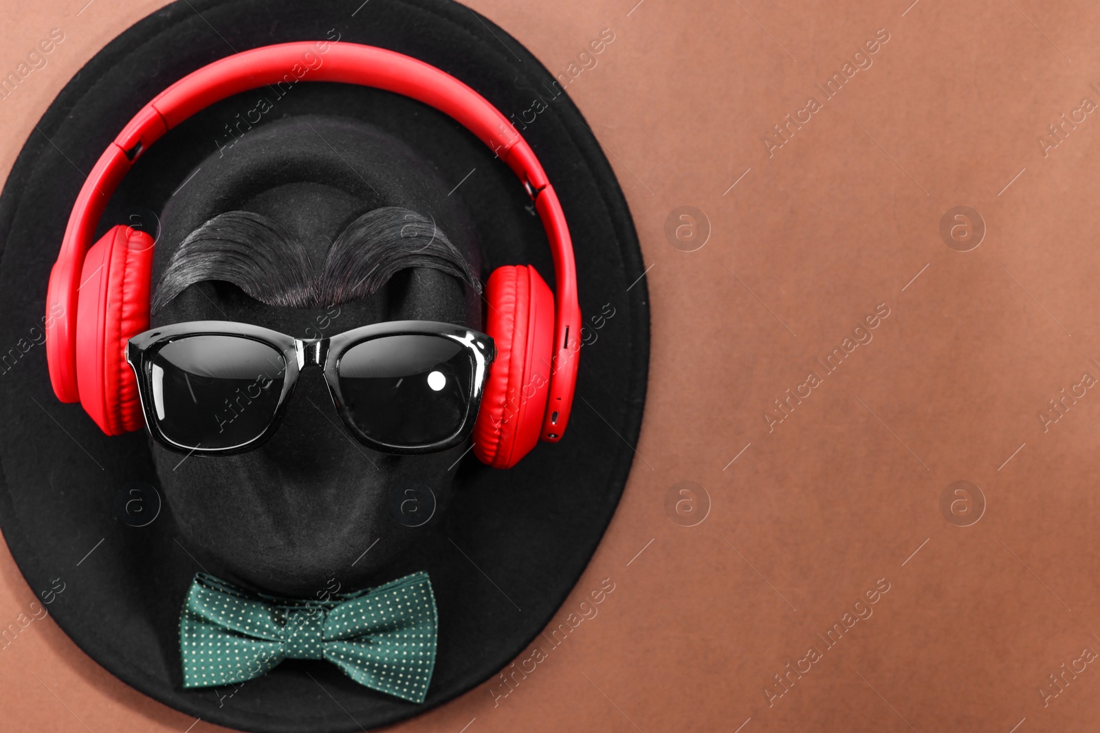 Photo of Man's face made of artificial mustache, sunglasses and hat on brown background, top view. Space for text