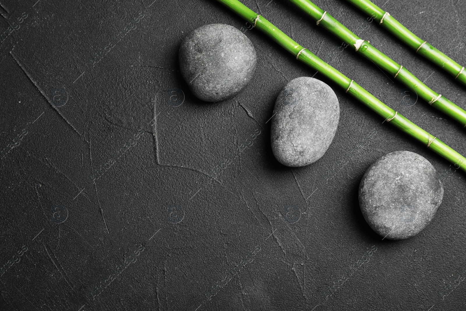 Photo of Zen stones and bamboo on dark background, top view with space for text