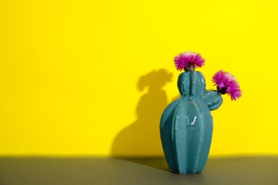 Trendy cactus shaped ceramic vase with flowers on table against color background