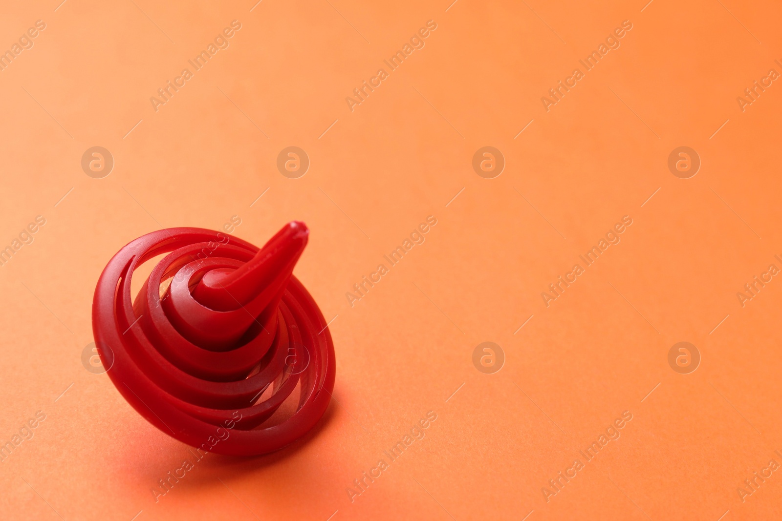 Photo of One red spinning top on orange background, closeup. Space for text