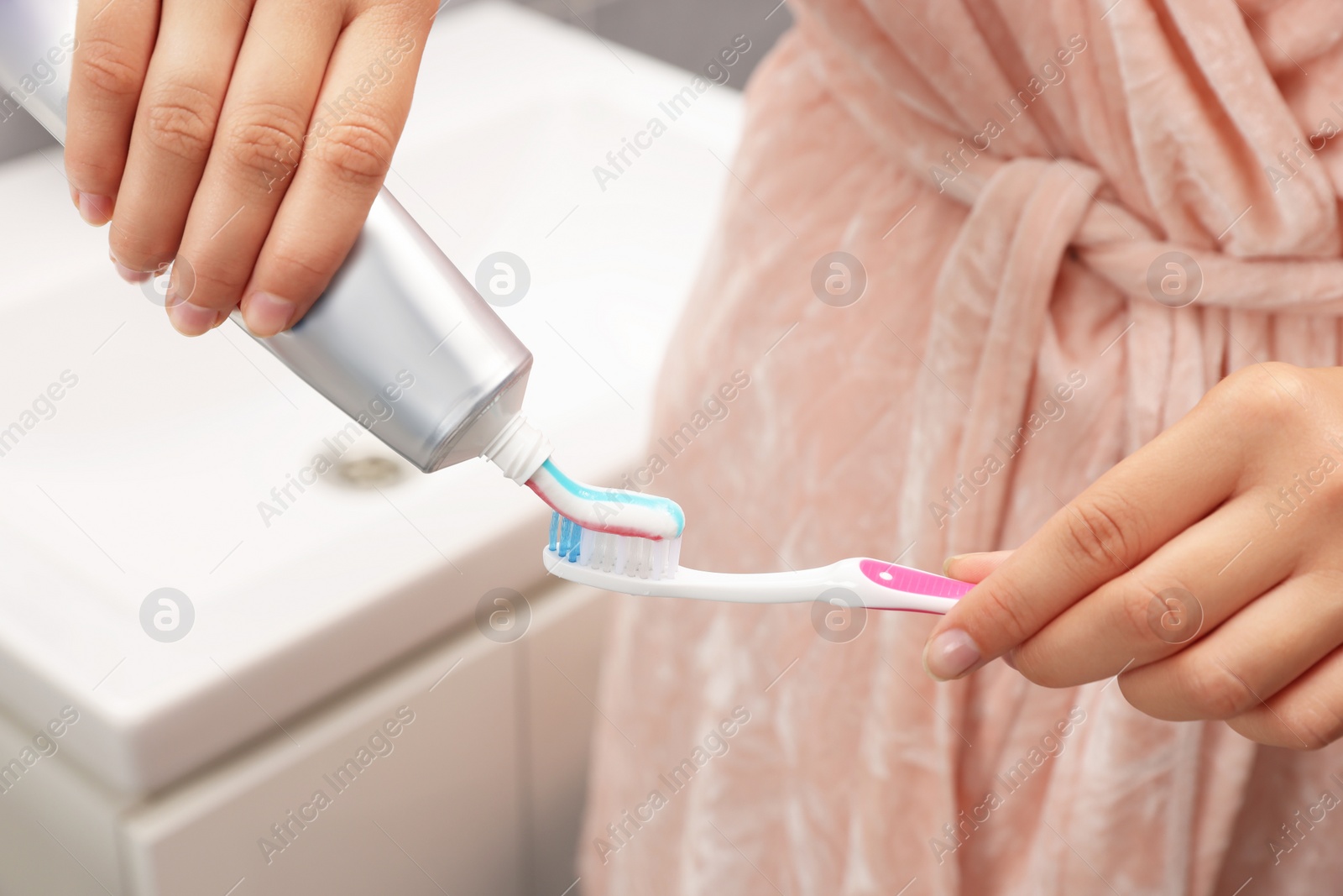 Photo of Woman applying toothpaste on brush in bathroom, closeup