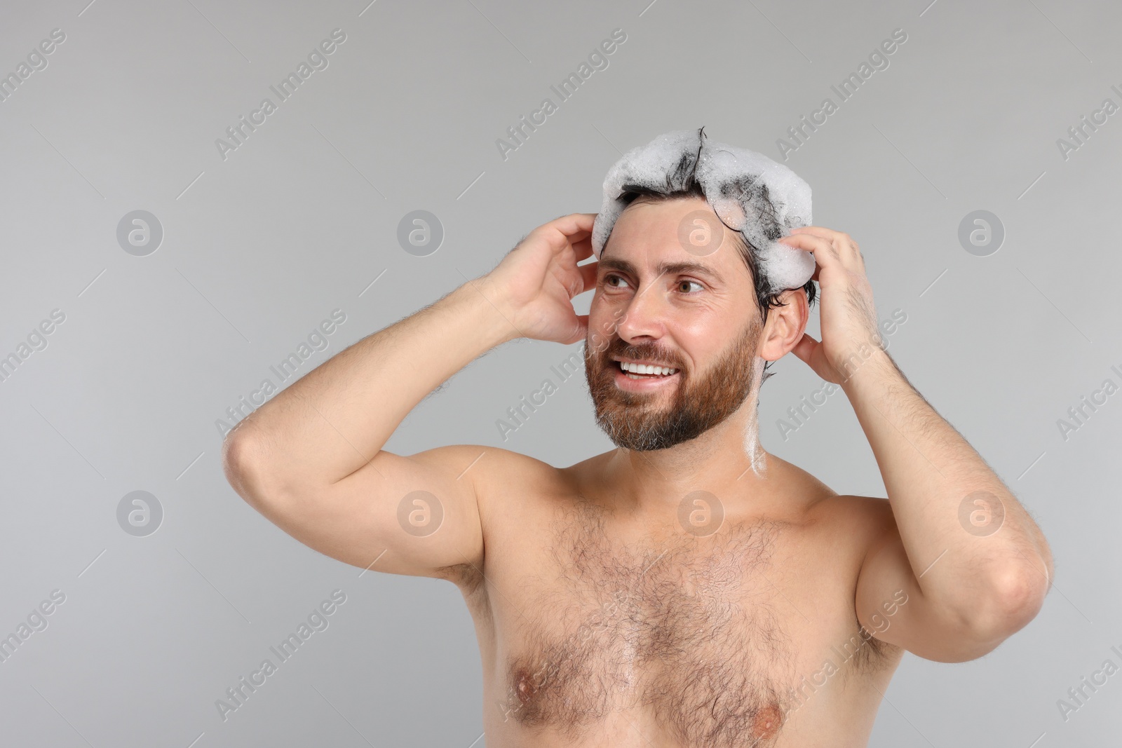 Photo of Happy man washing his hair with shampoo on grey background