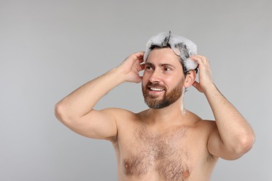 Happy man washing his hair with shampoo on grey background