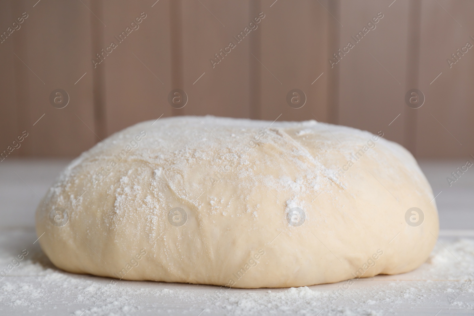 Photo of Fresh yeast dough with flour on white wooden table, closeup