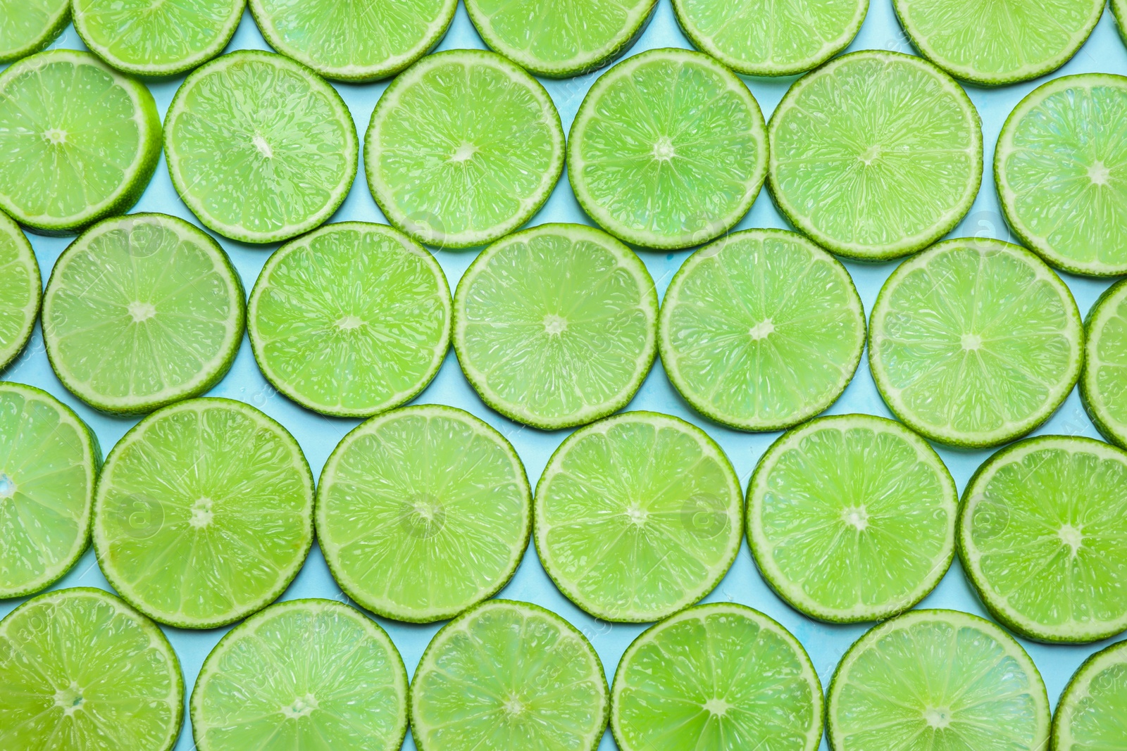 Photo of Juicy fresh lime slices on light blue background, flat lay