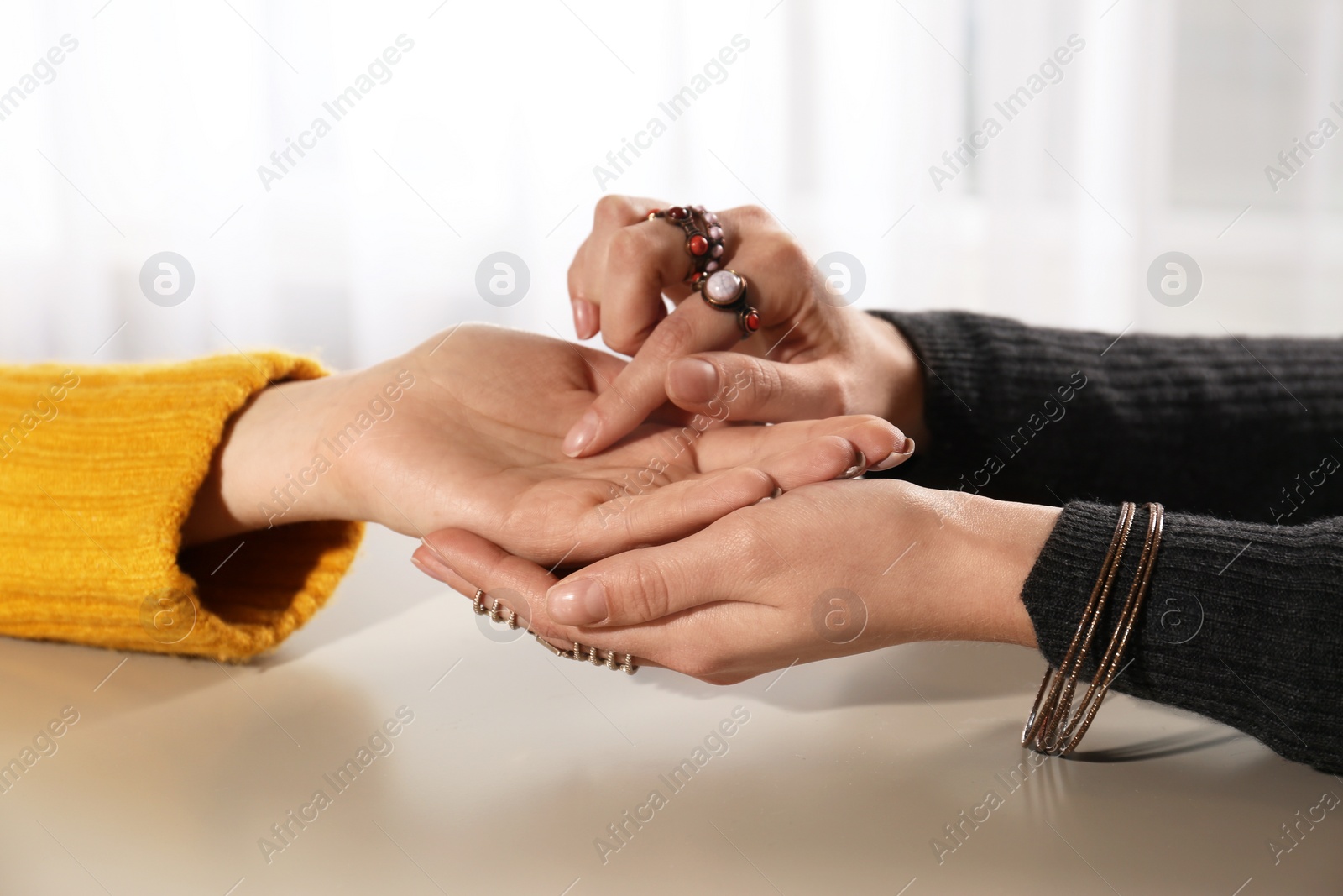 Photo of Chiromancer reading lines on woman's palm at table, closeup