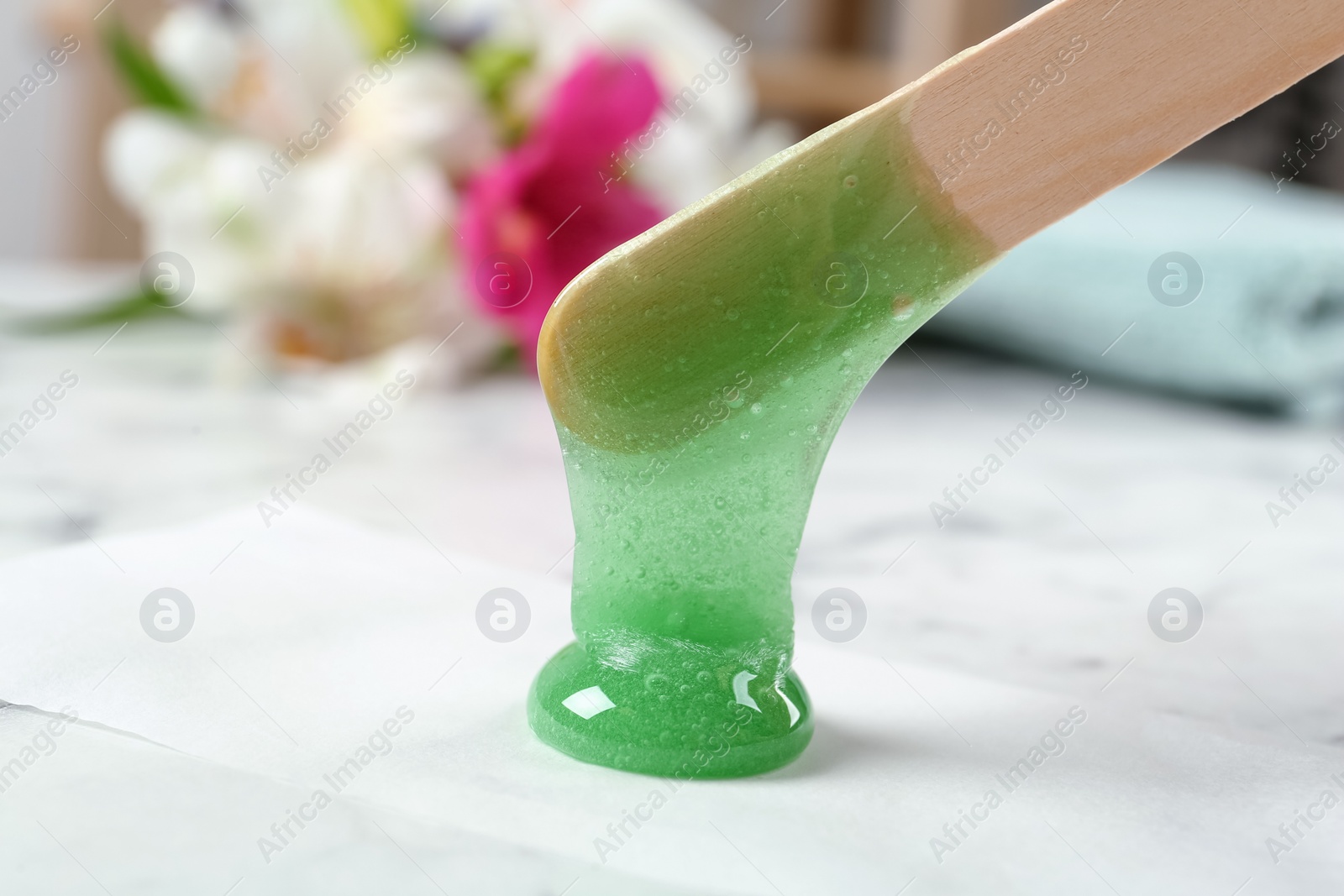 Photo of Applying wax on paper with spatula at white marble table, closeup