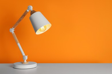 Stylish modern desk lamp on white table near orange wall, space for text