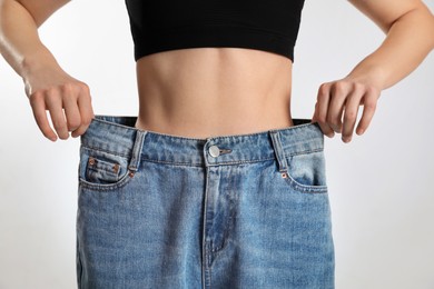 Photo of Skinny woman in oversized jeans on light background, closeup. Weight loss concept