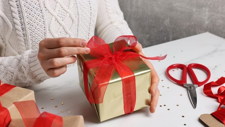 Photo of Woman wrapping Christmas gift at white marble table, closeup
