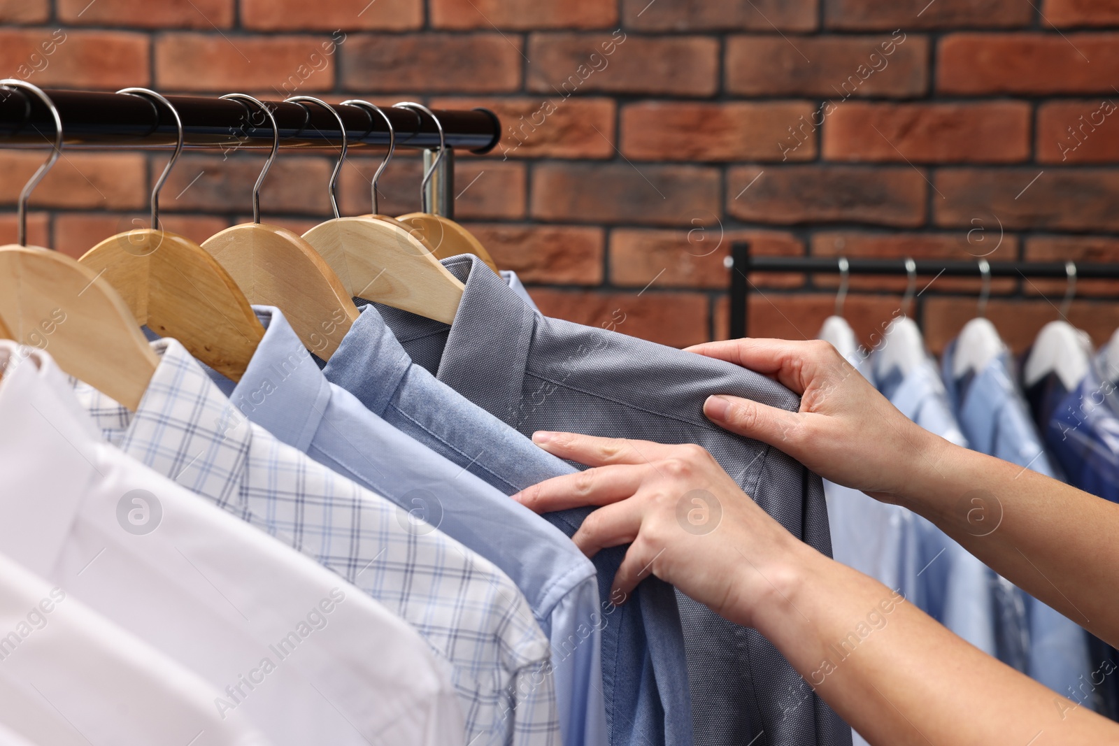 Photo of Dry-cleaning service. Woman taking shirt from rack against brick wall, closeup