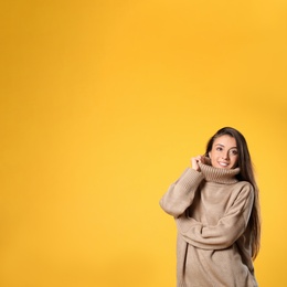 Young woman in stylish brown sweater on yellow background, space for text