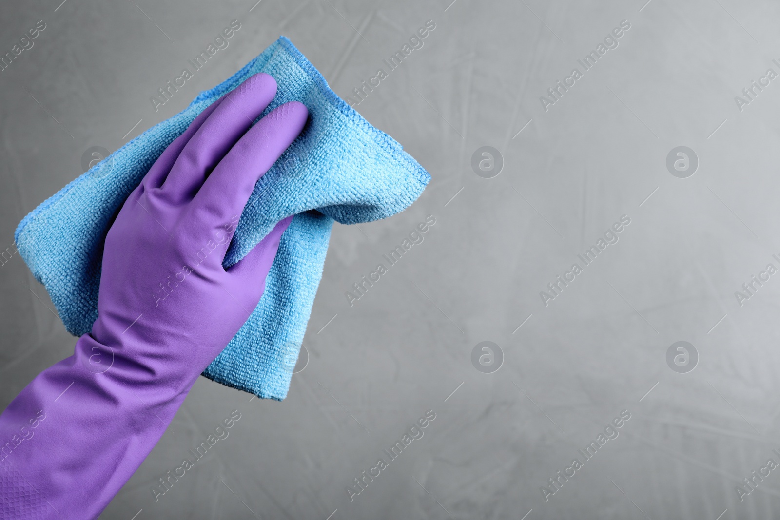 Photo of Woman in violet rubber gloves with microfiber cloth on light grey background, closeup. Space for text