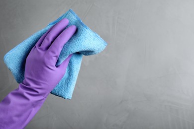 Woman in violet rubber gloves with microfiber cloth on light grey background, closeup. Space for text