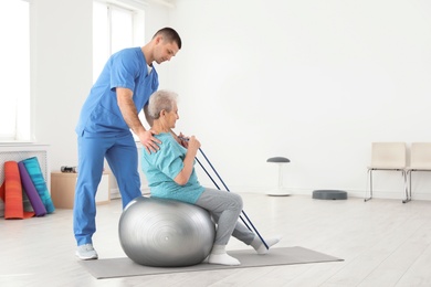 Professional physiotherapist working with elderly patient in rehabilitation center. Space for text