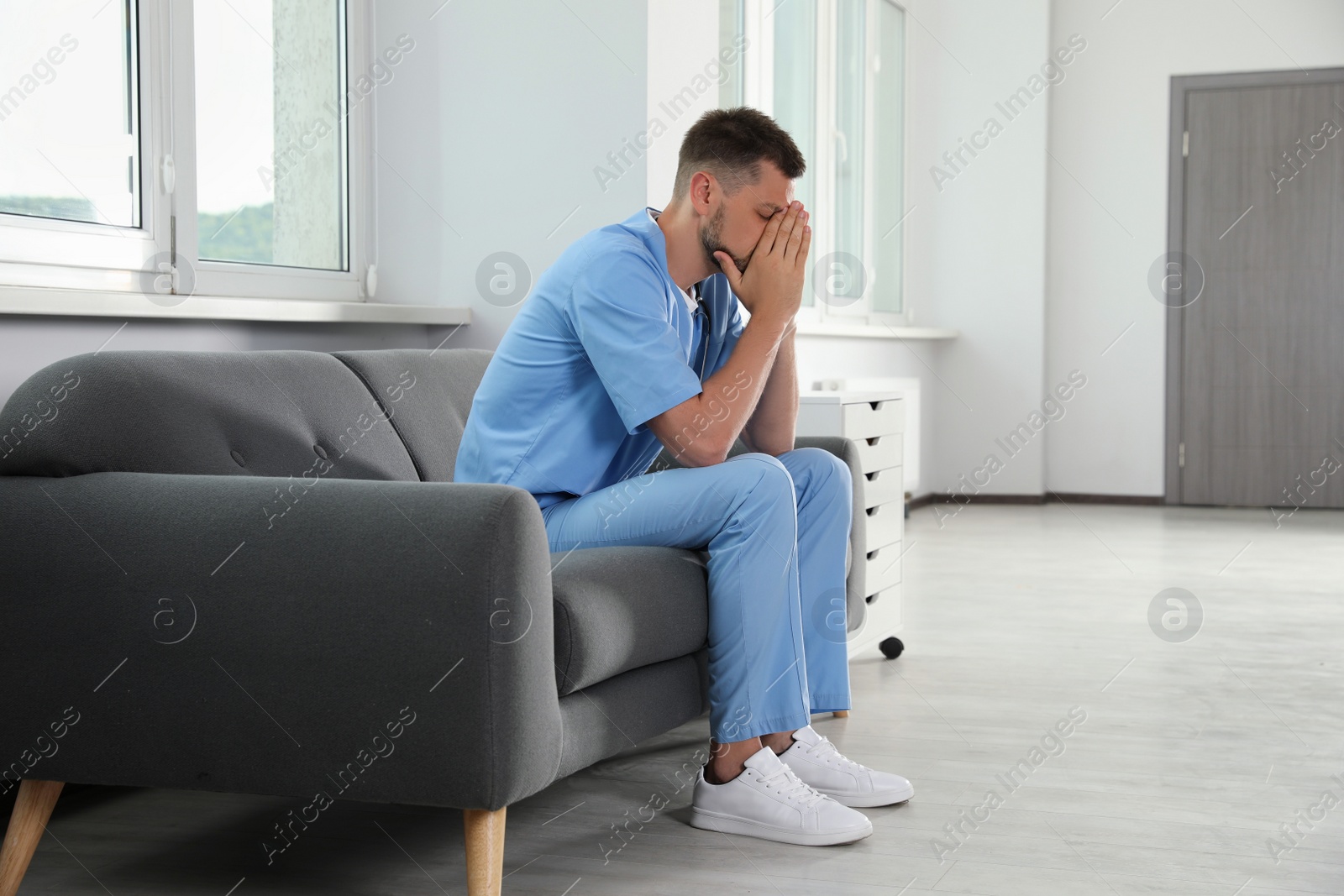 Photo of Exhausted doctor sitting on sofa in hospital