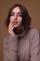 Portrait of beautiful young woman in warm sweater on brown background