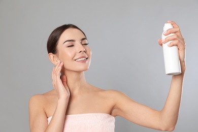 Photo of Young woman applying thermal water on face against grey background. Cosmetic product